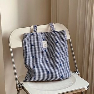 Detail of blue and white gingham tote bag with delicate floral embroidery on fabric