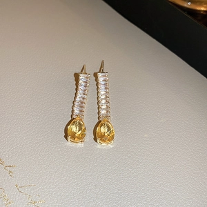 Détail de boucles d'oreilles dorées à pompons avec cristaux jaunes et zircons brillants