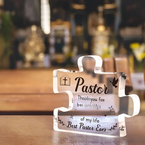 Close-up of puzzle-shaped acrylic plaque with Best Pastor Ever text on a wooden background