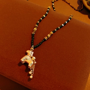 Detail van tijgeroog kralenketting met gouden schaap hanger en elegante kwastjes