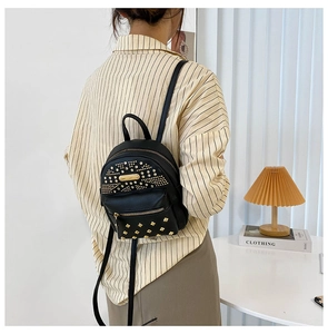 Detail view of a black PU leather backpack with gold rivets and metallic plaque on model