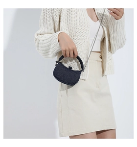 Detail view of a navy blue denim handbag featuring a silver chain strap worn by a model