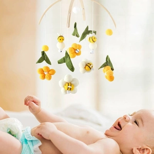 Detail of wooden baby mobile featuring felt bees and flowers hanging over a smiling infant