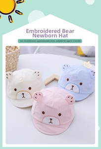 Detailed view of newborn cotton caps with bear embroidery in white, pink, and blue