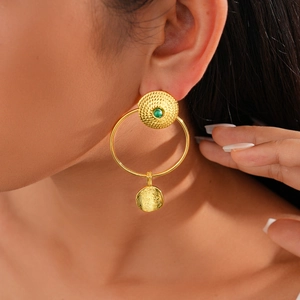 Close-up of gold earrings with green gemstone and hammered texture on a model