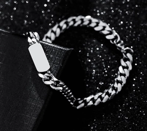 Close-up of a silver titanium Cuban chain bracelet with a blank engraving plate on a black box