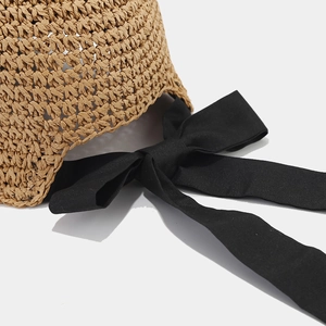 Close-up of hand-woven straw hat texture featuring a large decorative black fabric bow