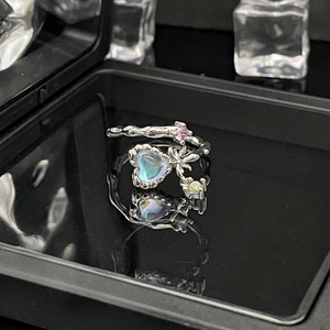 Macro shot of silver bow ring with heart moonstone and colorful gems on dark surface
