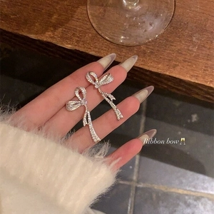 Close-up of sparkling bow earrings with micro-set zircons held against a cozy sweater