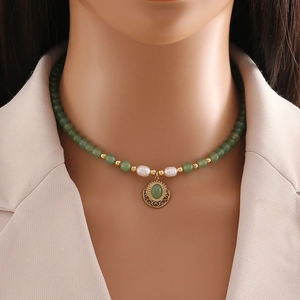 Handmade necklace with green jade beads, pearls, and a vintage gold pendant on a model