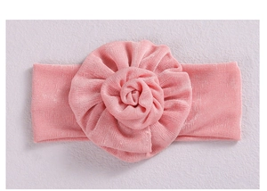 Detail of pink knitted cotton baby headband with a large 3D flower on a grey background