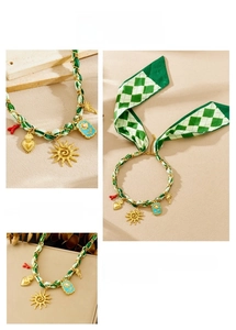 Detail of silk ribbon and gold chain necklace with sun and flower charms on beige background