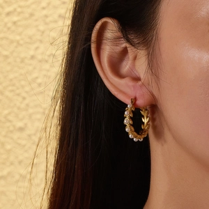 Close-up of golden hoop earrings with pearl accents worn by a model in warm light