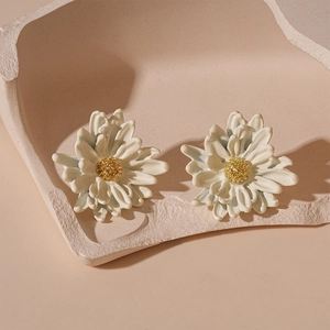 Detail of white flower stud earrings with golden pistils on a textured stone base