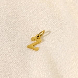 Detailaufnahme eines goldenen Z-Anhängers auf funkelndem beigem Stoffhintergrund