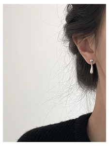Close-up of liquid metal silver teardrop stud earrings worn on a model ear