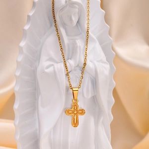 Detailed view of a gold cross pendant necklace displayed on a white religious statue