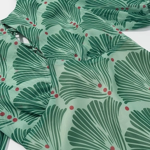 Detailed close-up of green chiffon dress with ginkgo leaf patterns and red polka dots
