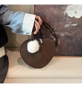 Nahaufnahme der braunen herzförmigen Wildledertasche mit weißem Bommel und Silber-Zipper