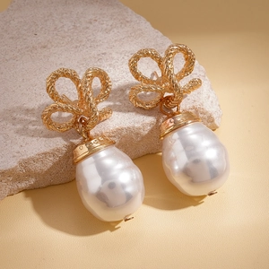 Retro gold bow knot and baroque pearl drop earrings displayed on a natural mineral stone