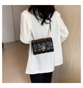 Close-up of black quilted chain shoulder bag on white blazer shown on a model