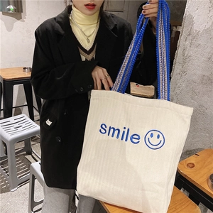 Detail of white corduroy tote bag showing blue smile embroidery and woven handles