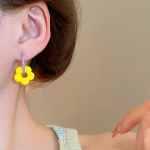 Close-up of a floral earring with yellow petals and purple hoop worn by a model