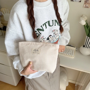 Close-up of a beige corduroy makeup pouch held by a person in a natural home setting