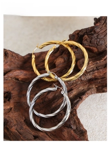 Detailed view of large gold and silver twisted hoop earrings on a rustic wood branch