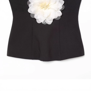 Haut tube noir ajusté avec une grande fleur blanche en 3D sur un fond blanc minimaliste