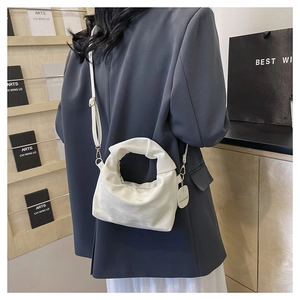 Detailed view of white pleated crescent bag with detachable strap and fashion charm
