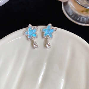 Macro view of blue star earrings with teardrop crystal pendants on ceramic tray
