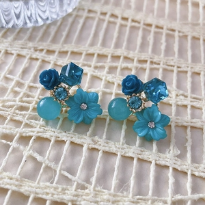 Macro detail of blue resin flower and crystal stud earring on white lace background