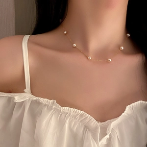 Detailed view of a gold-plated necklace with white freshwater pearls on a woman's collarbone