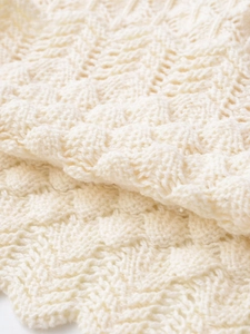 Detail of soft cream knitted fabric featuring unique wavy cutout hollow-out patterns