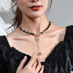 Detail of gold T-bar necklace with black woven leather chain and pearl tassel