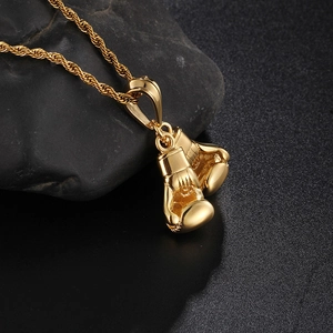 Polished gold boxing glove pendant with twist chain on natural black stone surface