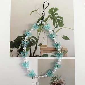 Detail von blauem Schmetterling und Perlen-Handykette auf künstlerischem Hintergrund