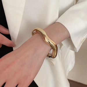 Close-up of a chunky irregular golden wave bangle with a polished mirror finish on a wrist
