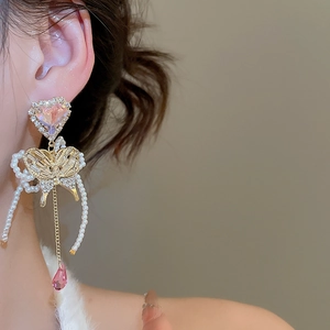 Macro view of butterfly earrings with pink crystals and pearls on a model's ear