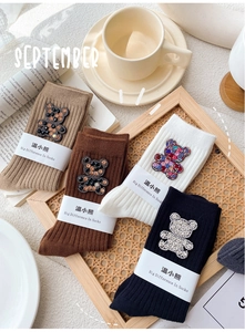 Detail of four-color knit socks featuring rhinestone bear patches in a rattan tray