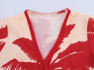 Close-up of V-neckline with red braided trim and tropical leaf print on beige fabric