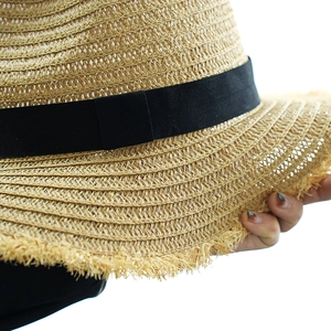 Close-up of beige straw sun hat with black ribbon and frayed tassel edges