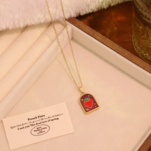 Detail view of heart-shaped enamel pendant on a golden chain displayed in a jewelry tray