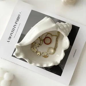 Detail of white ceramic conch jewelry tray holding golden daisy necklaces and rings