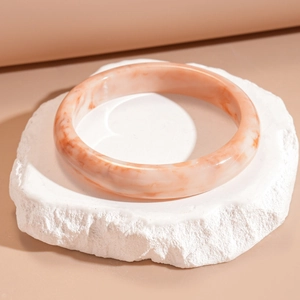 Gros plan d'un bracelet en résine marbrée orange sur base en pierre naturelle beige