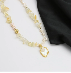 Detailed view of Baroque pearl pendant and yellow gemstone beads on a white background