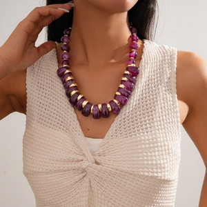 Close-up of purple irregular acrylic beads and gold metal rings on a beige sweater