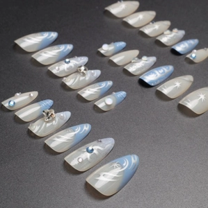 Faux ongles dégradé bleu avec nœuds 3D, perles et motifs étoilés pour manucure chic