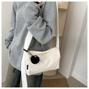 Detail showing white corduroy tote bag texture with a cute black pompom and wide strap